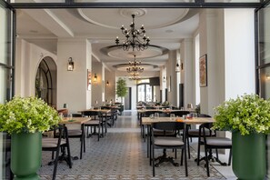 A spacious restaurant with high ceilings, chandeliers, and potted plants.