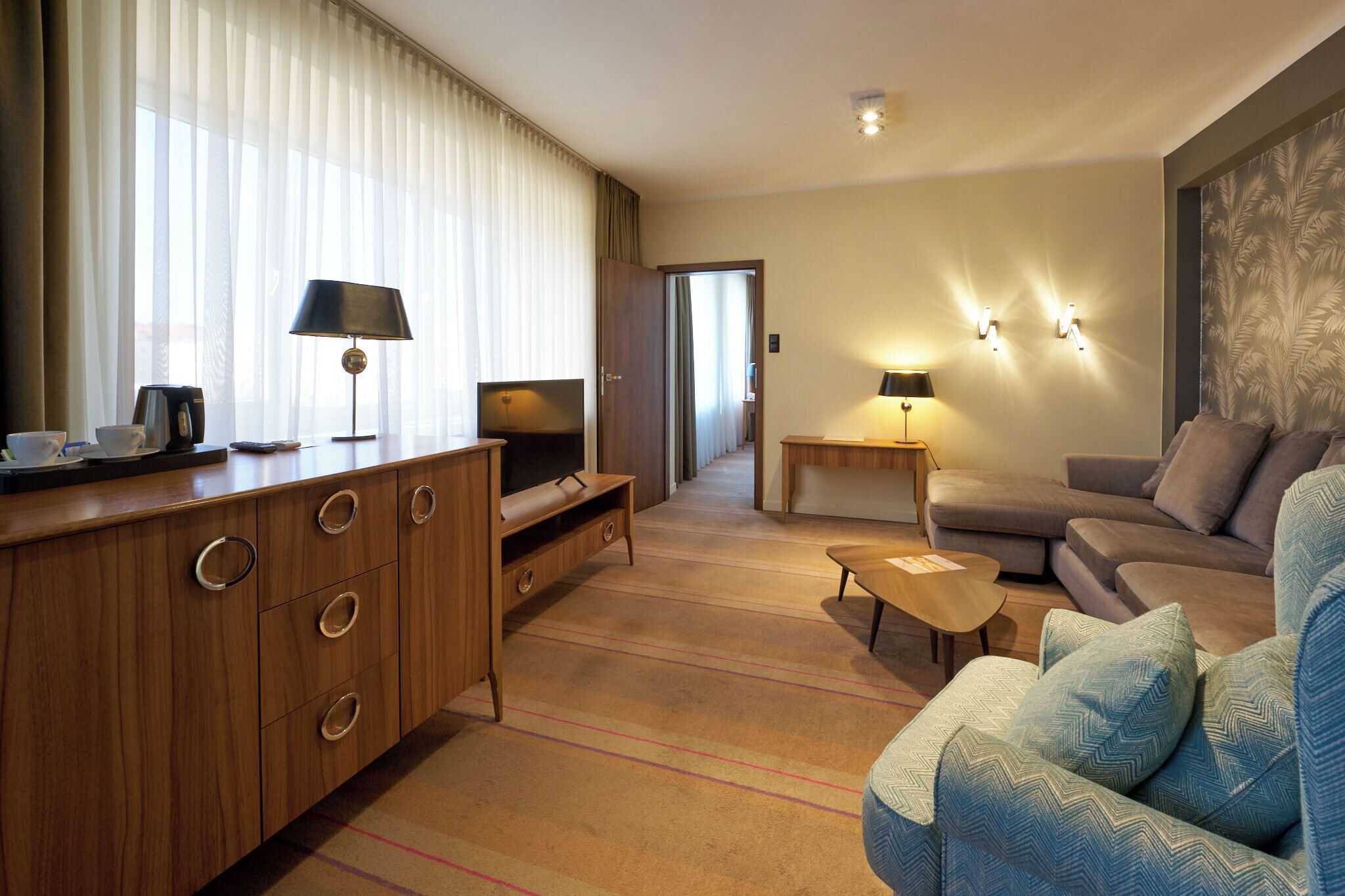 Quarto de hotel com armário de madeira, televisão, sofá e duas luminárias.
