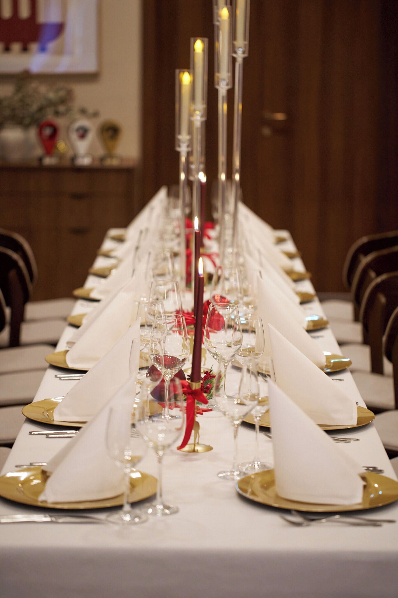A long dining table set with white tablecloths, gold and white napkins, and clear glassware.