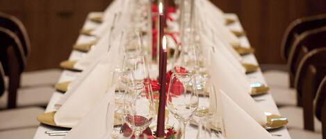 A long dining table set with white tablecloths, gold and white napkins, and clear glassware.