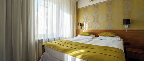 A hotel room with a bed, curtains, a wall with a pattern, a nightstand, and a lamp.