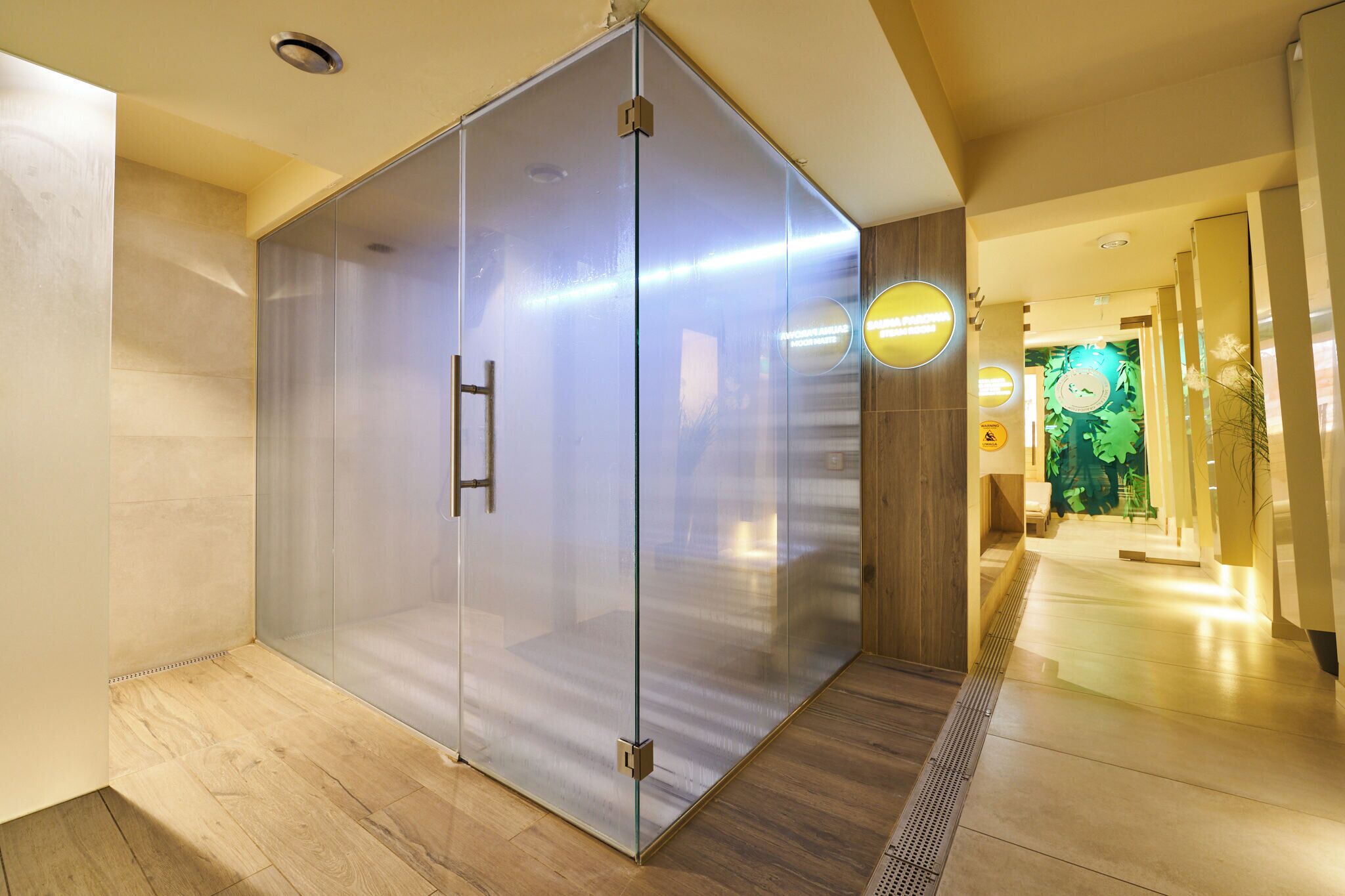 A modern hotel corridor with a glass partition, wooden flooring, and a visible elevator.