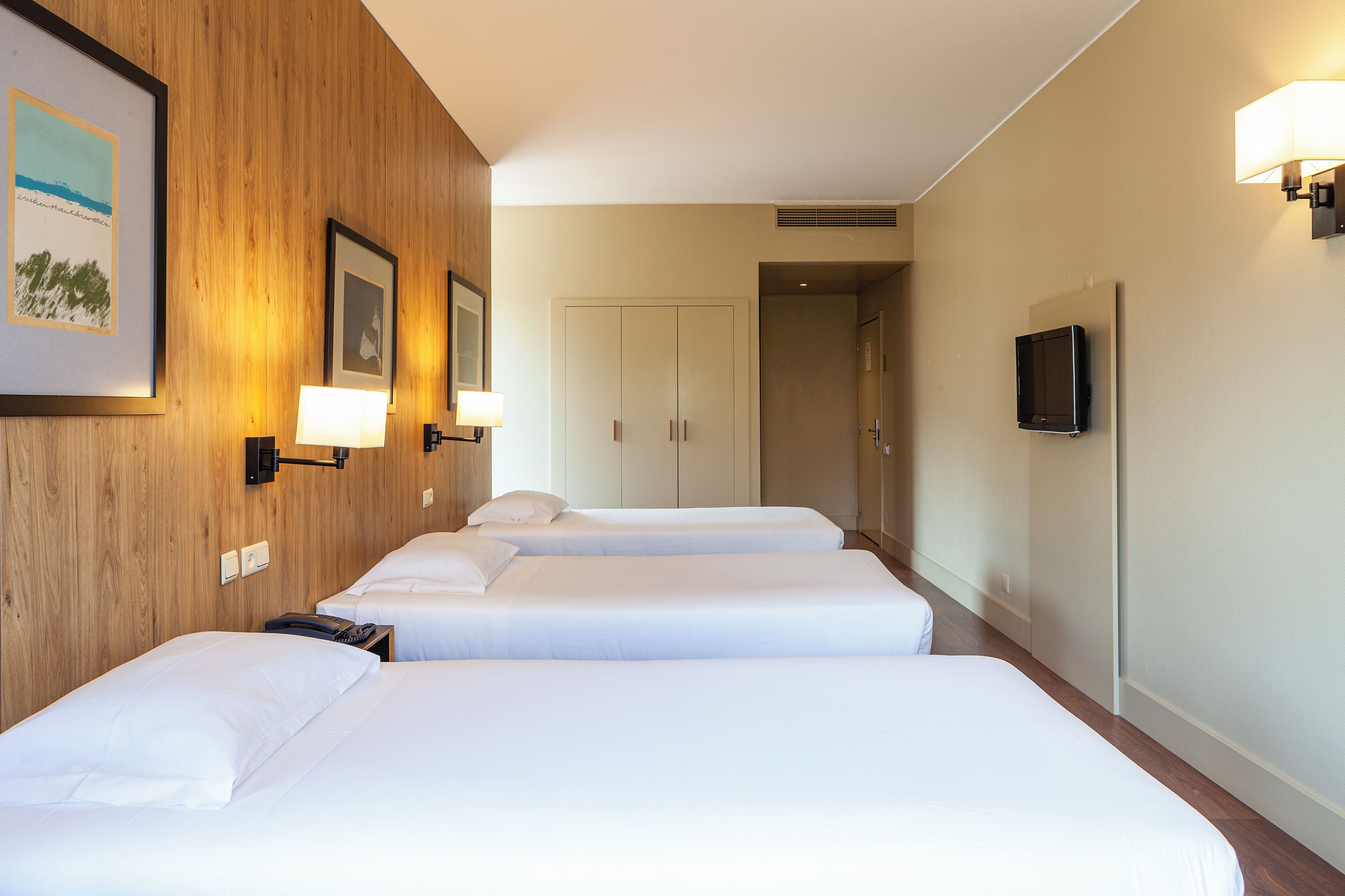 A hotel room with three beds, wooden paneling, a TV, and framed artwork on the wall.