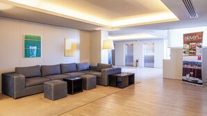 Un espace lounge moderne comprenant un canapé d’angle, des poufs et un bar avec un présentoir de menus.