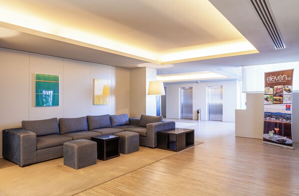 A modern lounge area with a sectional sofa, ottomans, and a bar area with a menu display.