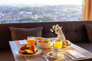 A breakfast table with croissants, a bowl of fruit, and orange juice, set on a balcony with a city view.