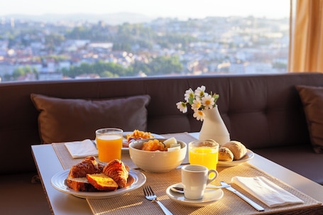 A breakfast table with croissants, a bowl of fruit, and orange juice, set on a balcony with a city view.