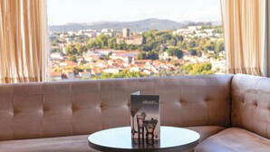 Un espace salon confortable avec des fauteuils, une table, un menu et une vue sur la ville par la fenêtre.
