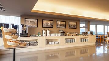 A modern hotel lobby with a buffet area, framed pictures on the wall, and a seating area with tables and chairs.