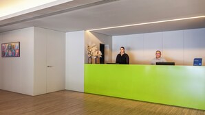 Un comptoir d’accueil avec un plan de travail vert, une œuvre d’art encadrée accrochée au mur et un panneau indiquant un espace d’attente.