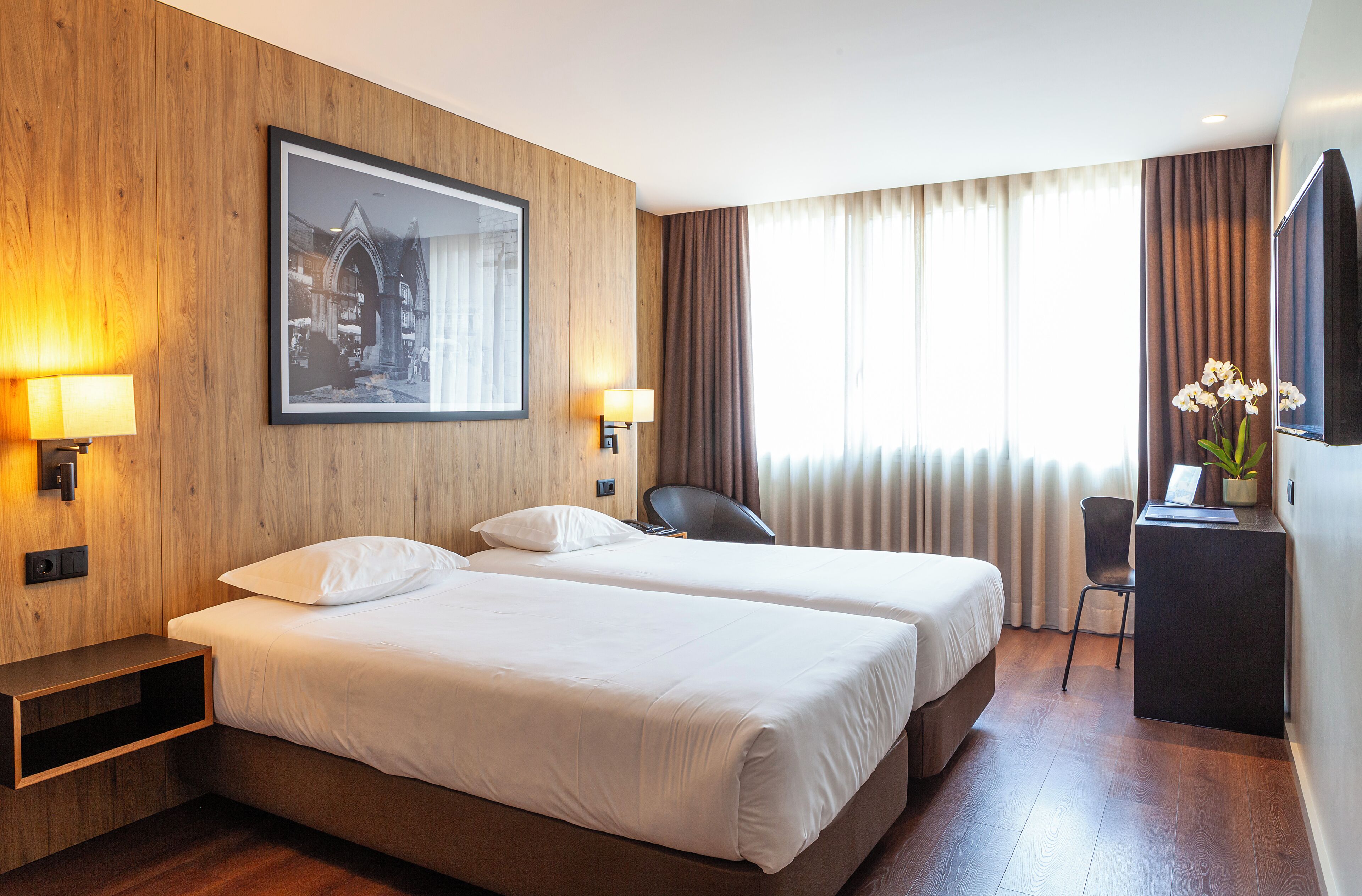 Habitación de hotel con dos camas, un escritorio, una silla, un televisor y un cuadro en la pared.