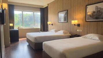 A hotel room with two beds, a desk, a chair, a lamp, and a window with curtains.
