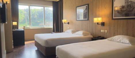A hotel room with two beds, a desk, a chair, a lamp, and a window with curtains.