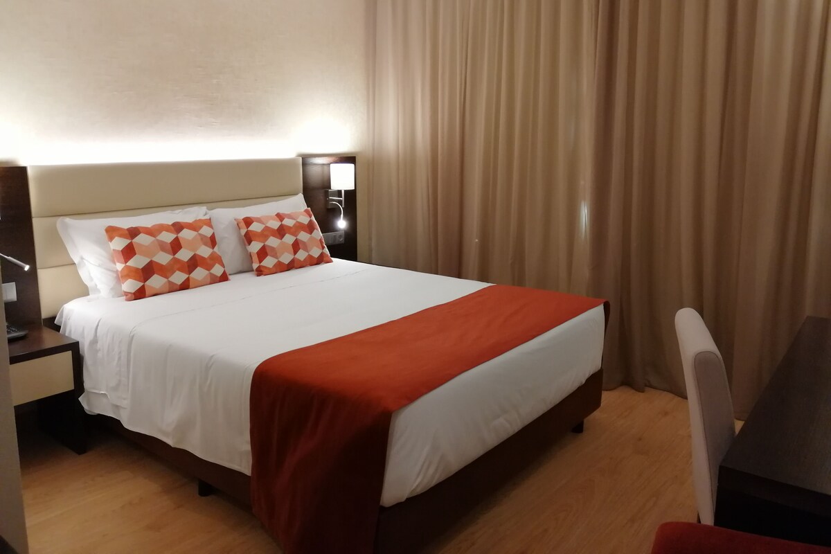 Una habitación de hotel con cama, mesita de noche, escritorio y silla.