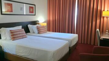 A hotel room with two beds, a desk, a chair, and a lamp.