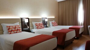 A hotel room with three beds, each with a red blanket and a patterned pillow. The room has a wooden floor and beige walls. - Hotel Mónaco (Faro)