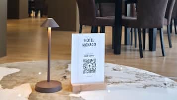 Un hall d’hôtel avec un comptoir de réception en marbre, un code QR donnant accès au menu de l’hôtel, et une table avec des chaises à l’arrière-plan.