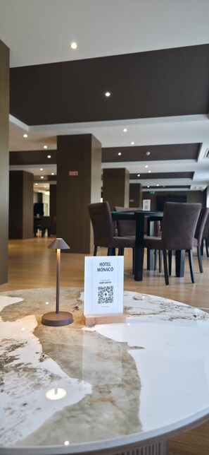 Un vestíbul d'hotel amb un taulell de recepció de marbre, un codi QR per al menú de l'hotel i una taula amb cadires al fons.