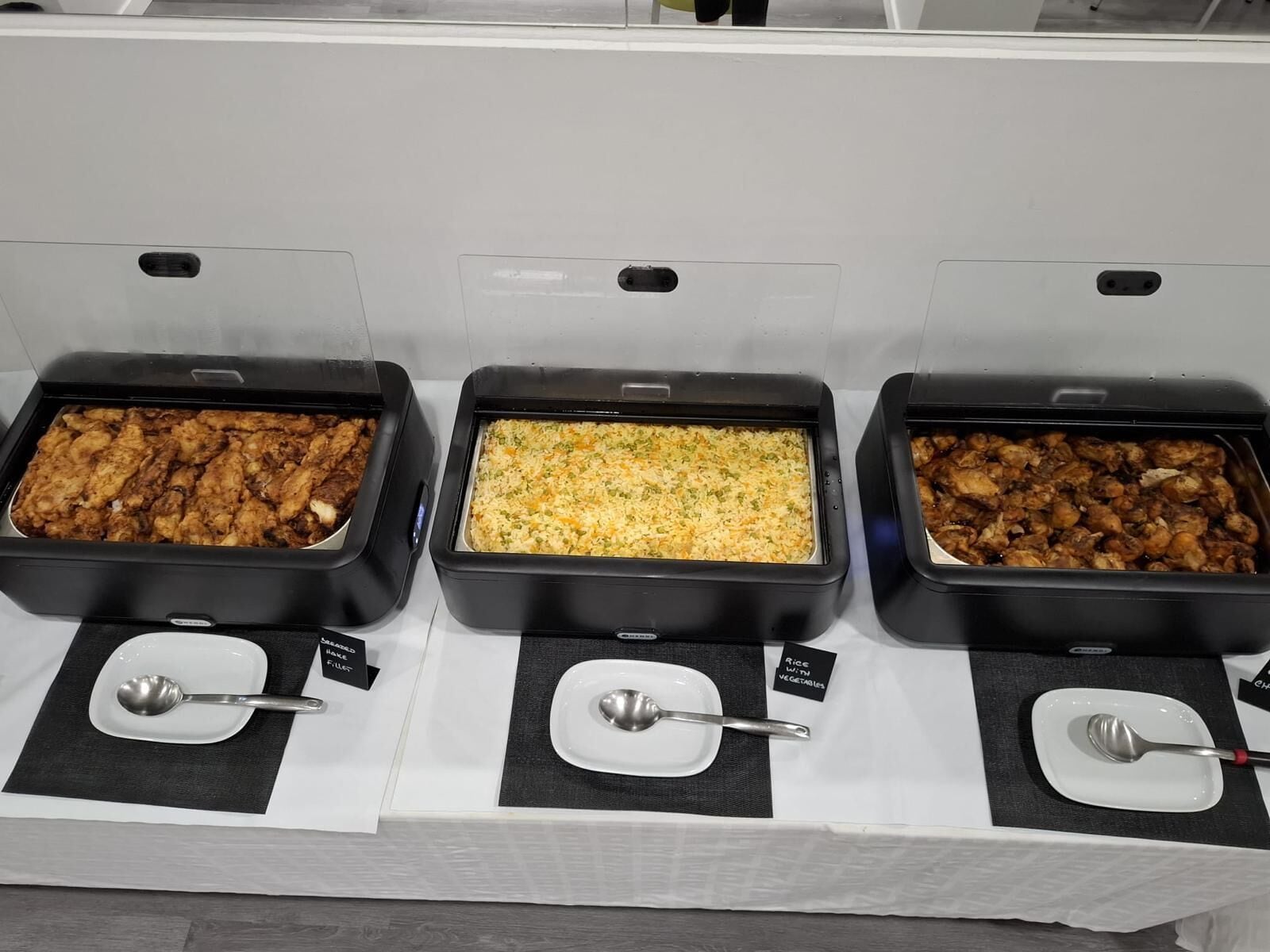 Un buffet comportant trois plateaux de nourriture, chacun étant étiqueté avec le nom d’un plat différent.