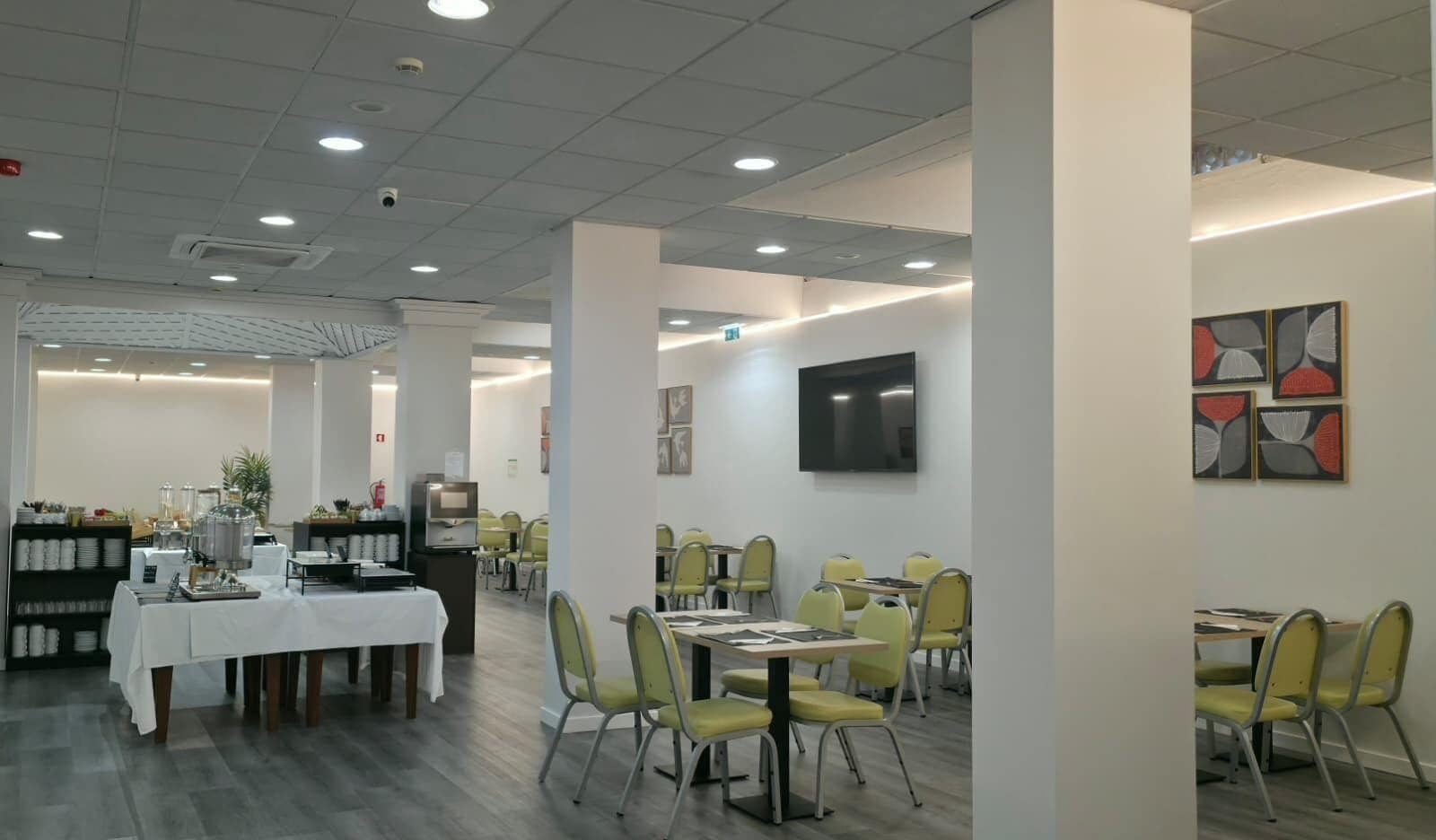 Un comedor con mesas y sillas, una barra de buffet y un televisor en la pared.