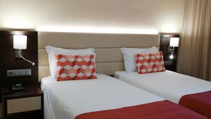 A hotel room with two beds, each with a red and white patterned pillow, a bedside table with a lamp, and a telephone. - Hotel Mónaco (Faro)