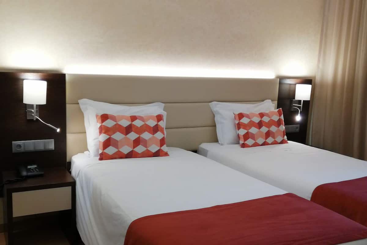 A hotel room with two beds, each with a red and white patterned pillow, a bedside table with a lamp, and a telephone.