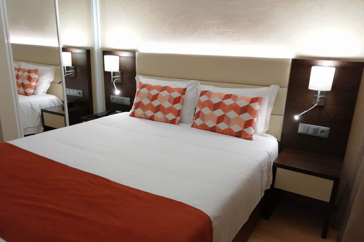 A hotel room with a large bed, two nightstands, a mirror, and a wall-mounted light.