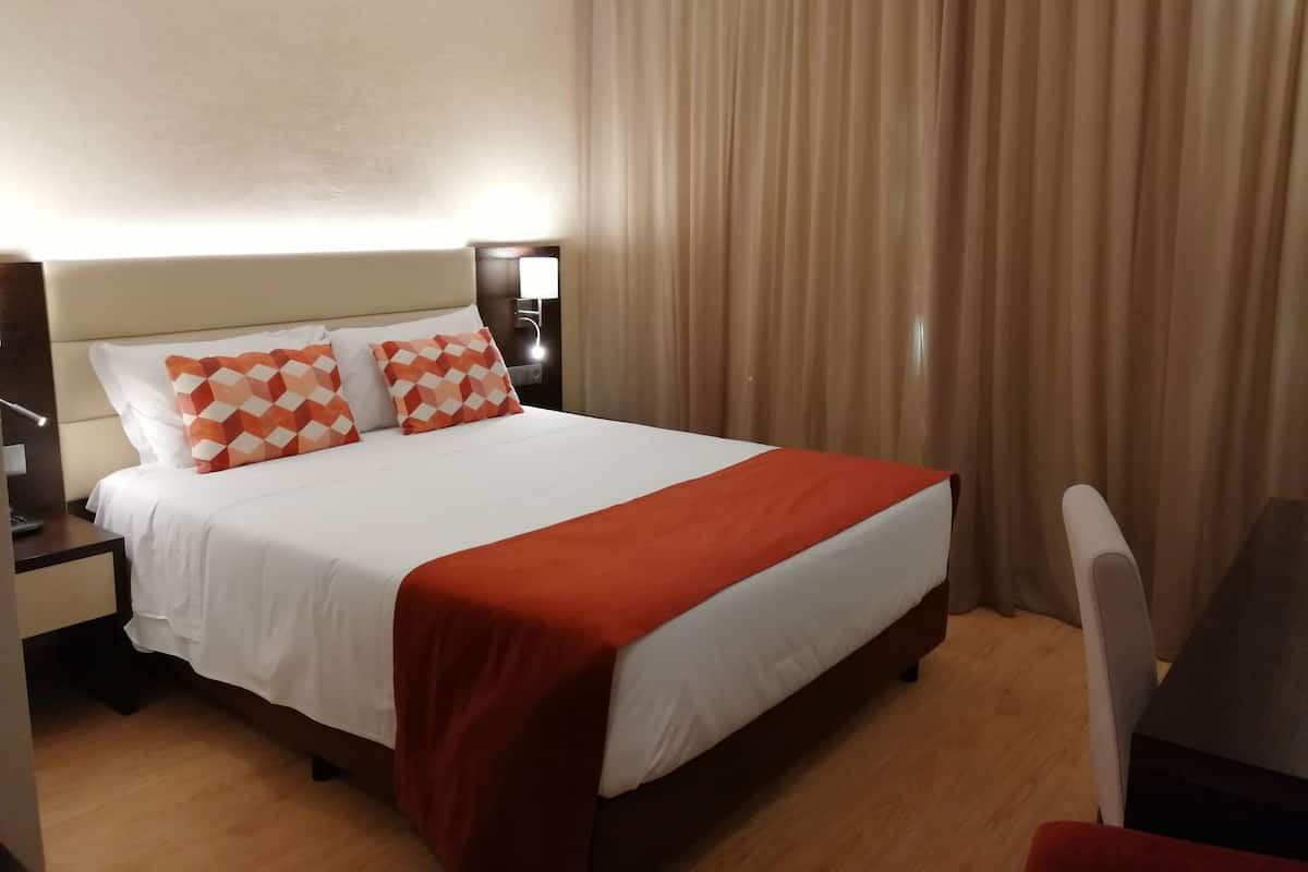 A hotel room with a bed, a nightstand, a desk, and a chair.