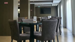 A modern dining area with a glass table and chairs, recessed ceiling lights, and a flat-screen TV mounted on the wall.