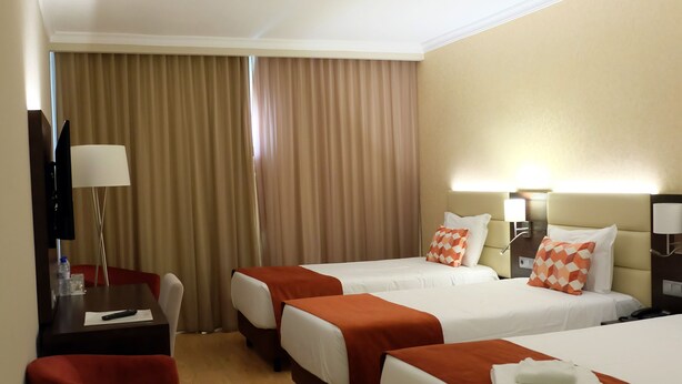 A hotel room with two beds, a desk with a chair, a TV, and a red ottoman. - Hotel Mónaco (Faro)