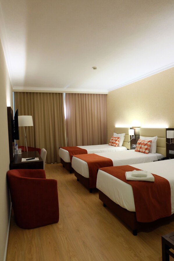 A hotel room with two beds, a desk with a chair, a TV, and a red ottoman. - Hotel Mónaco (Faro)