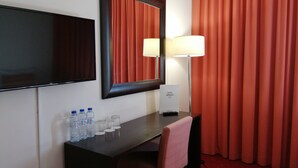 A hotel room with a desk, a flat-screen TV, a mirror, a lamp, a chair, and a red curtain. - Hotel Mónaco (Faro)