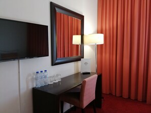 A hotel room with a desk, a flat-screen TV, a mirror, a lamp, a chair, and a red curtain. - Hotel Mónaco (Faro)