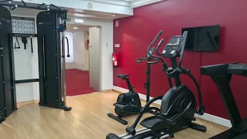 Ett gym med konditionsmaskiner, en stång för chins och en röd vägg.