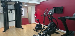 Ein Fitnessraum mit Cardiogeräten, einer Klimmzugstange und einer roten Wand.