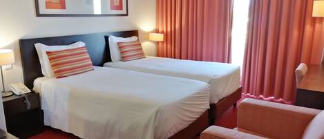 Una habitación de hotel con dos camas, un escritorio, una silla, un teléfono y un cuadro en la pared.