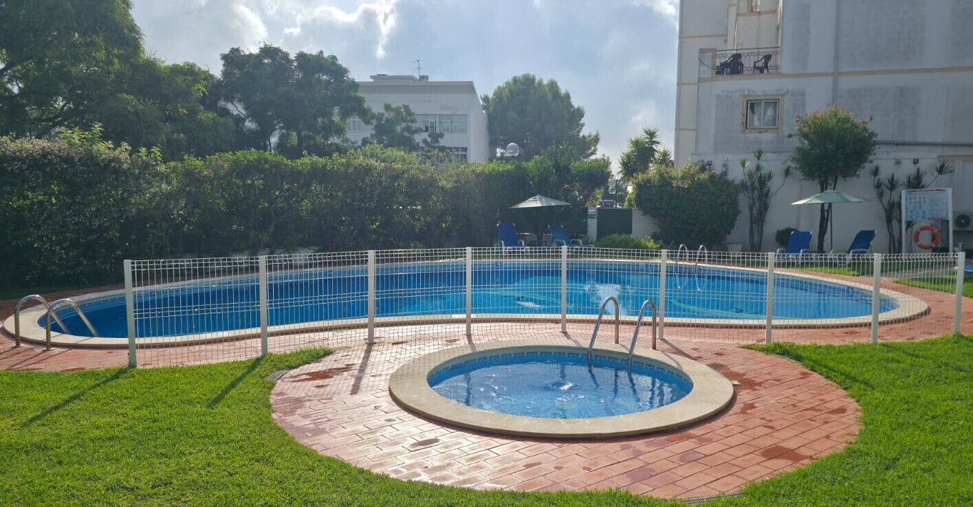 Ein Schwimmbecken mit umgebender Umzäunung, ein kleineres kreisförmiges Becken und eine Rasenfläche.