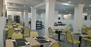 A modern dining area with yellow chairs and tables, white pillars, and a counter with a menu.