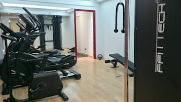 Uma academia com várias máquinas de exercícios, um banco e uma porta com a inscrição 'FAITTECH'.