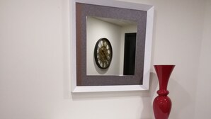 A white console table with a red vase and a framed clock on the wall above it. - Hotel Mónaco (Faro)