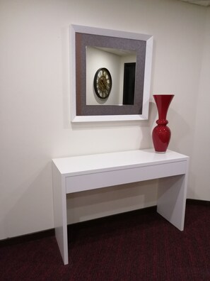 A white console table with a red vase and a framed clock on the wall above it. - Hotel Mónaco (Faro)
