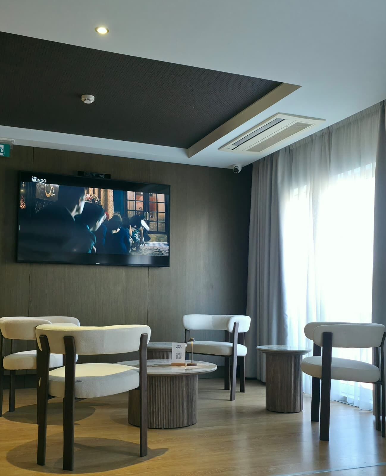 A modern living room with a flat-screen TV, comfortable seating, and a large window.