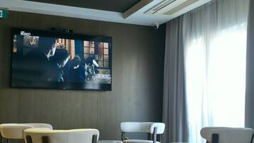 A modern living room with a flat-screen TV, comfortable seating, and a large window.
