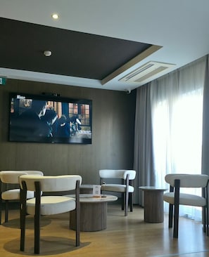A modern living room with a flat-screen TV, comfortable seating, and a large window.