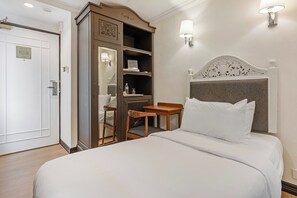 Una habitación de hotel con una cama, un armario de madera, una mesita pequeña y dos lámparas fijadas a la pared.