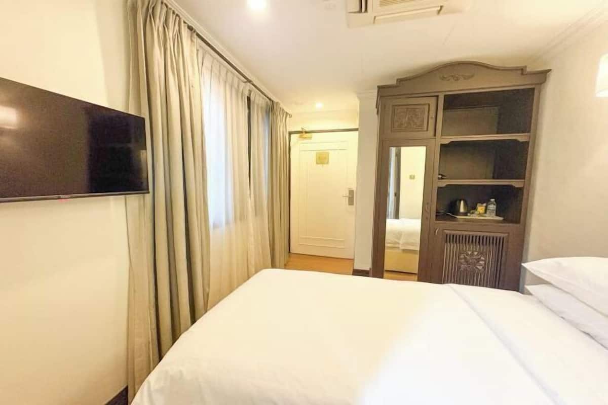 A hotel room with a bed, a television on the wall, a wardrobe, and a door leading to another room.