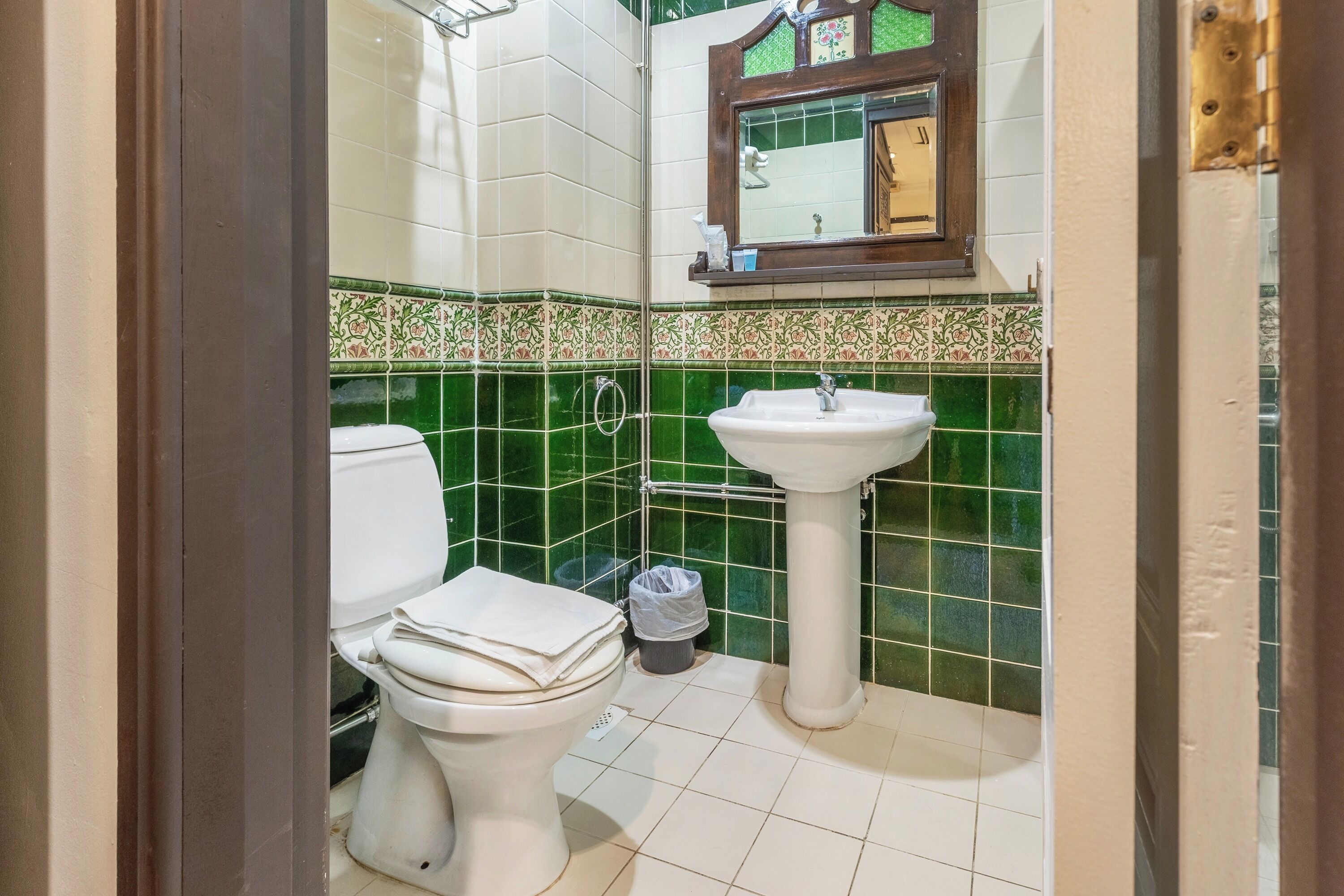 A bathroom with a toilet, sink, and green tiled walls.