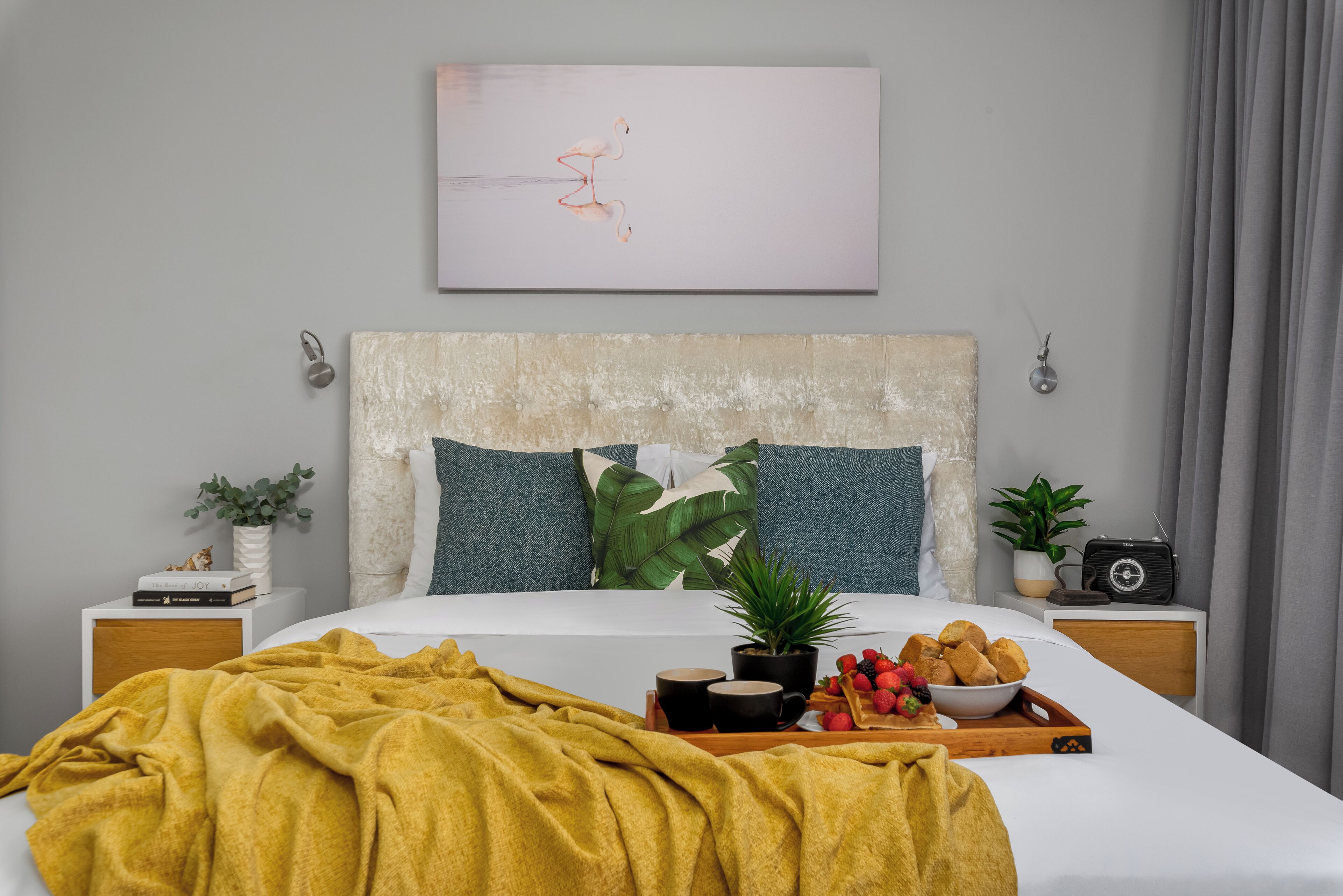 A neatly made bed with a mustard-colored blanket, a tray of breakfast items, and a radio on a bedside table.