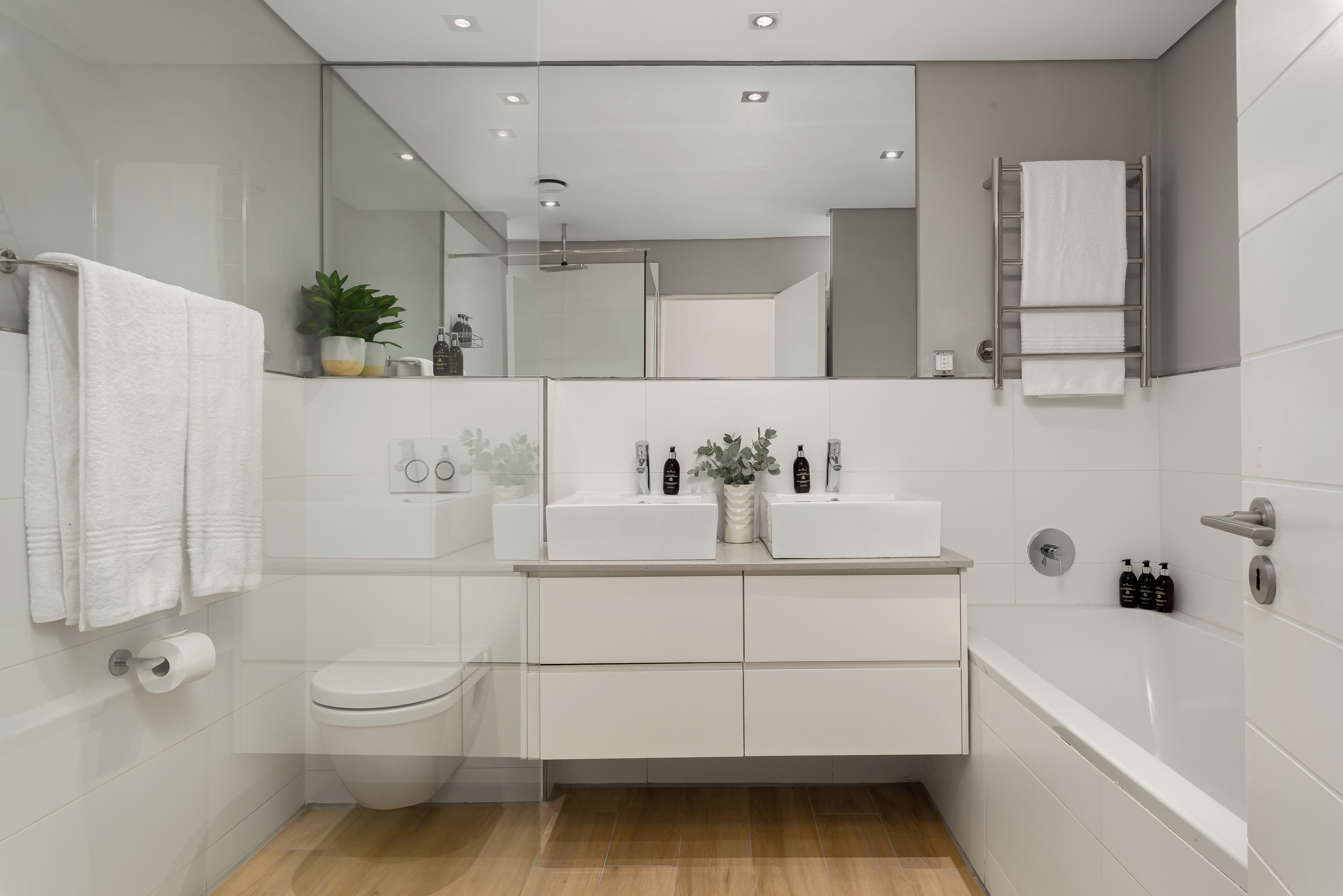 Une salle de bain moderne avec des toilettes, un lavabo et une baignoire. On y trouve des serviettes suspendues à un porte-serviettes, un miroir et une plante en pot sur le comptoir.