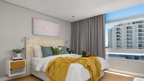 A modern bedroom with a large bed, a bedside table with a plant, a view of a cityscape through a window, and a city building in the background. - 24 Villa Marina (Cape Town)